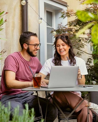 Studierende sitzen draussen in einem Kaffee, trinken etwas und arbeiten am Laptop.